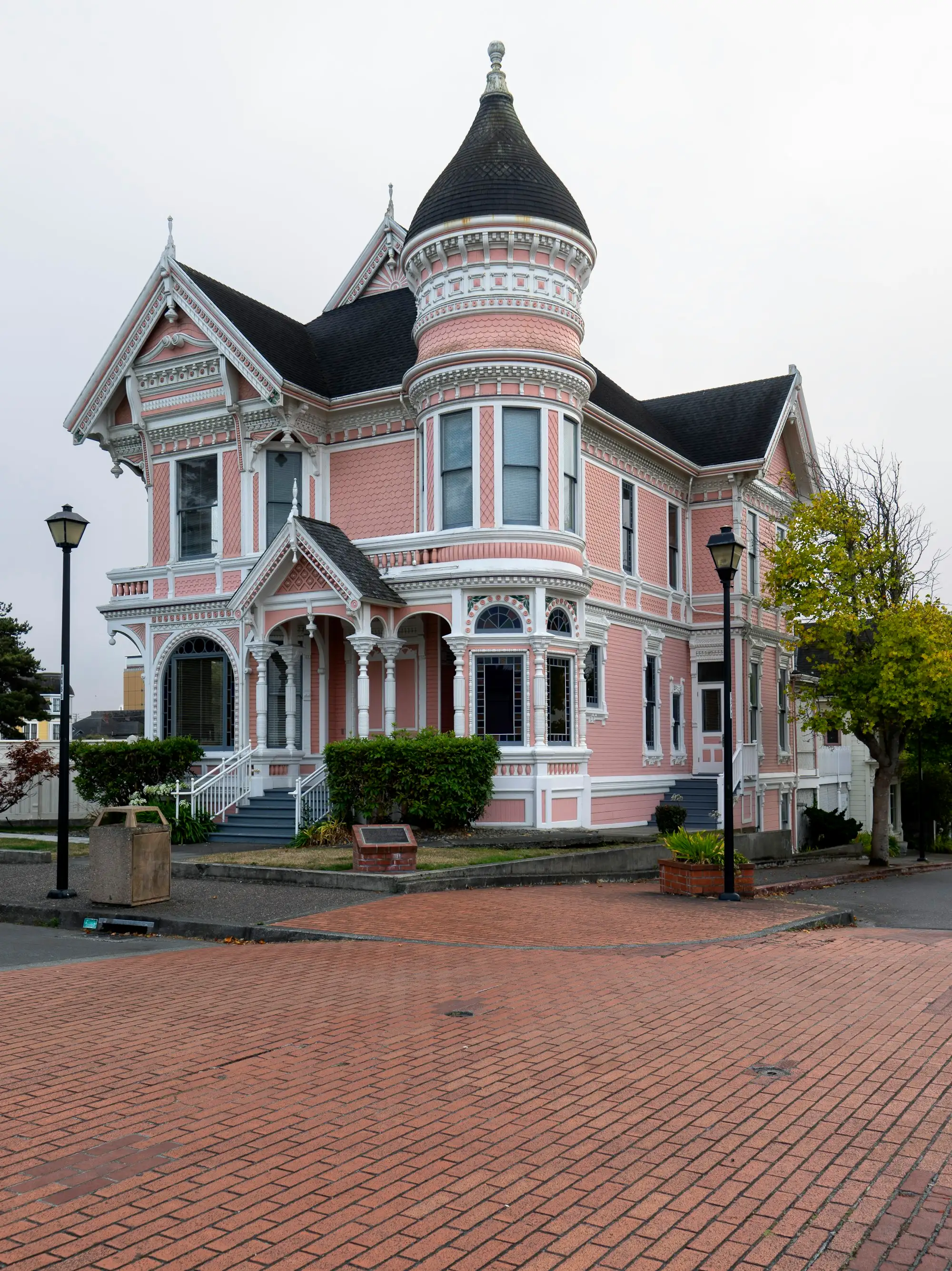 An ornate pink and white Victorian house with turrets and a lamppost-lined sidewalk