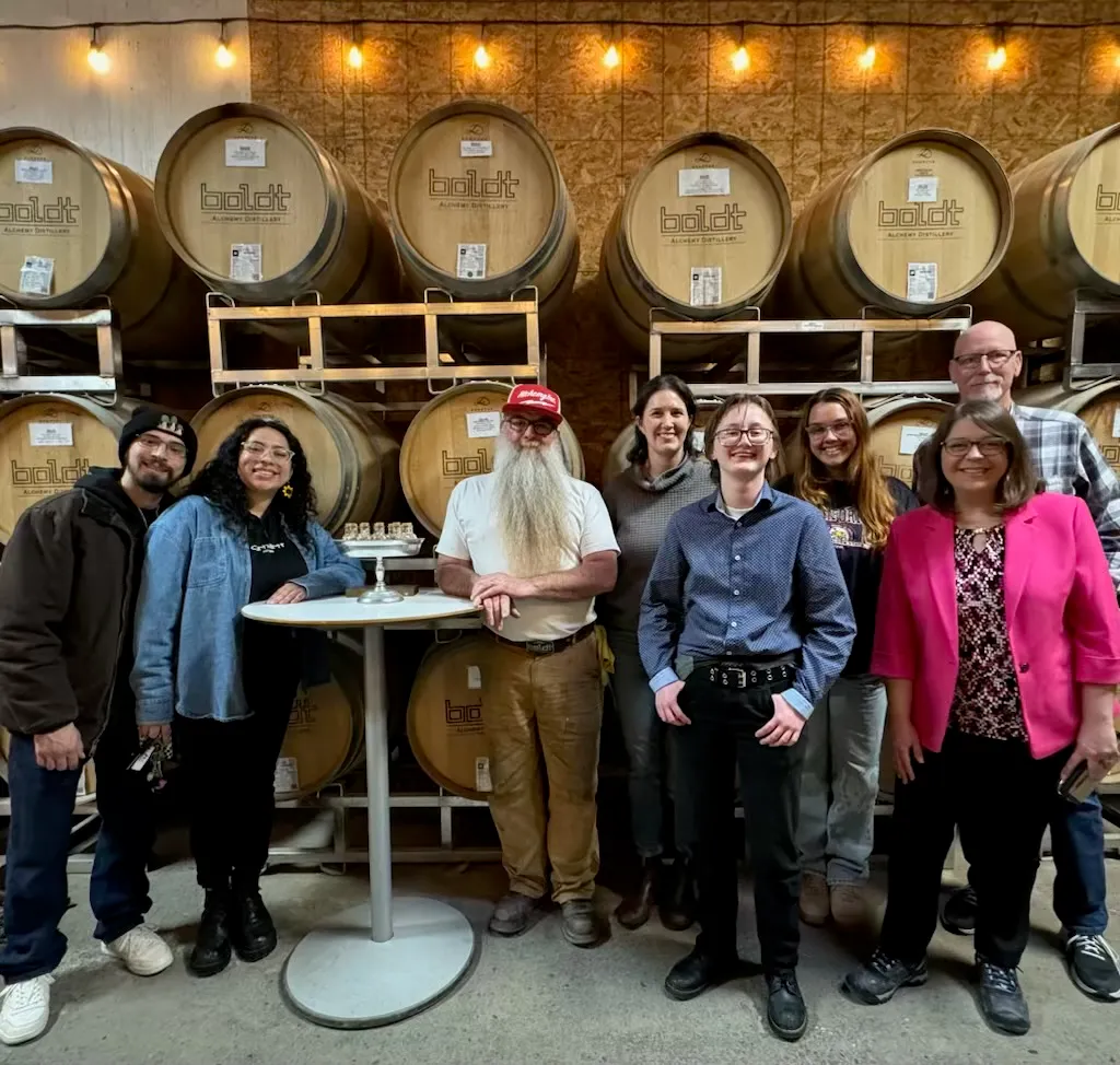 Arcata Chamber members on a field trip smile for a group photo in front of barrels of spirits at Boldt Alchemy Distillery