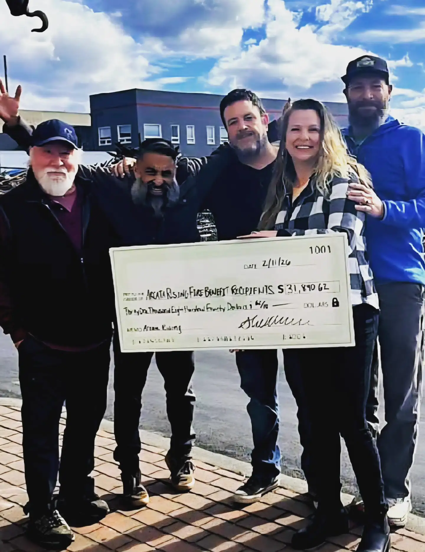Five people standing outdoors hold up a large donation check for Arcata fire relief recipients