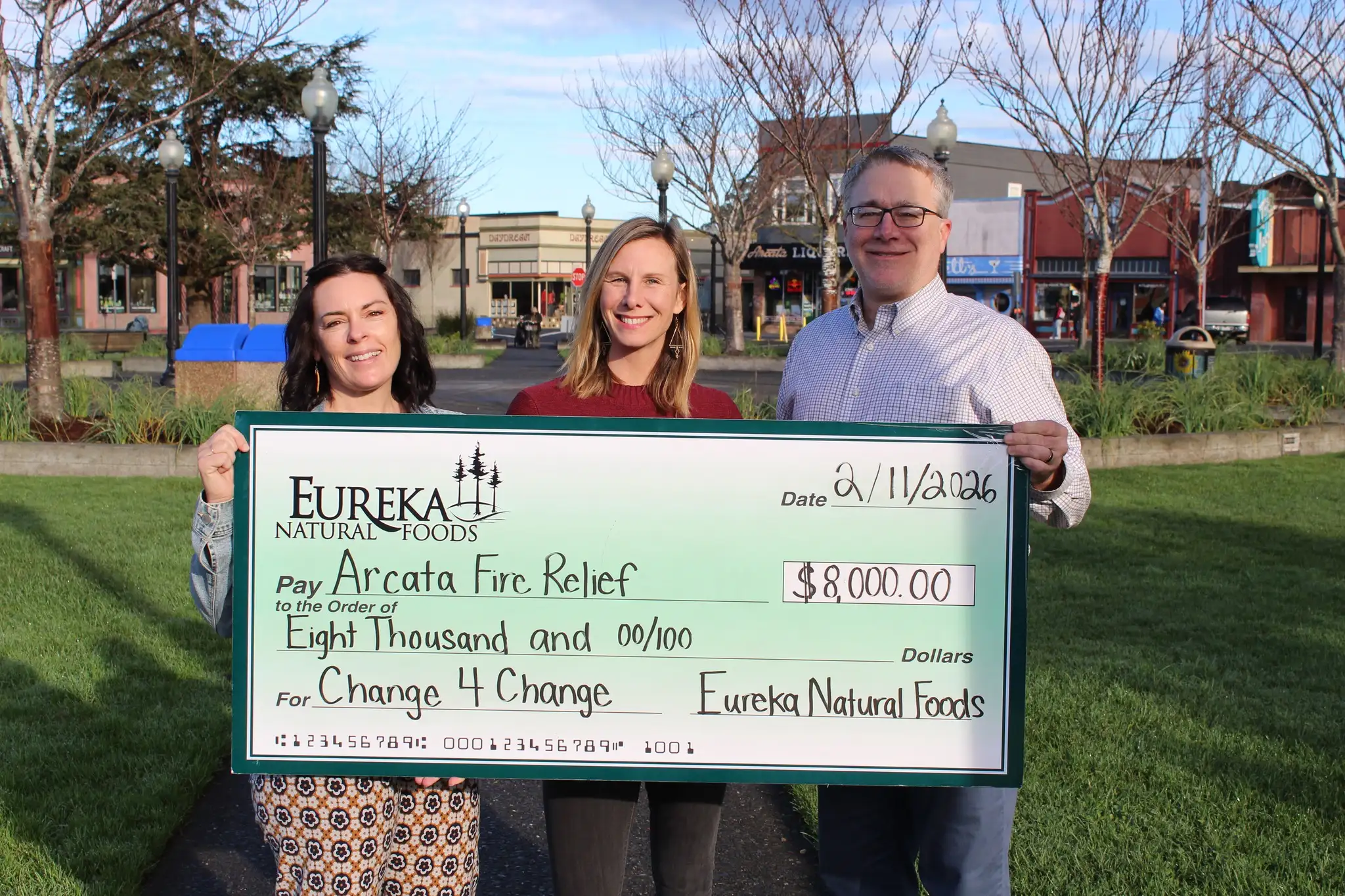 Three people on the Arcata Plaza hold an oversized $8,000 check from Eureka Natural Foods’ Change 4 Change program, made out to Arcata Fire Relief and dated February 11, 2026