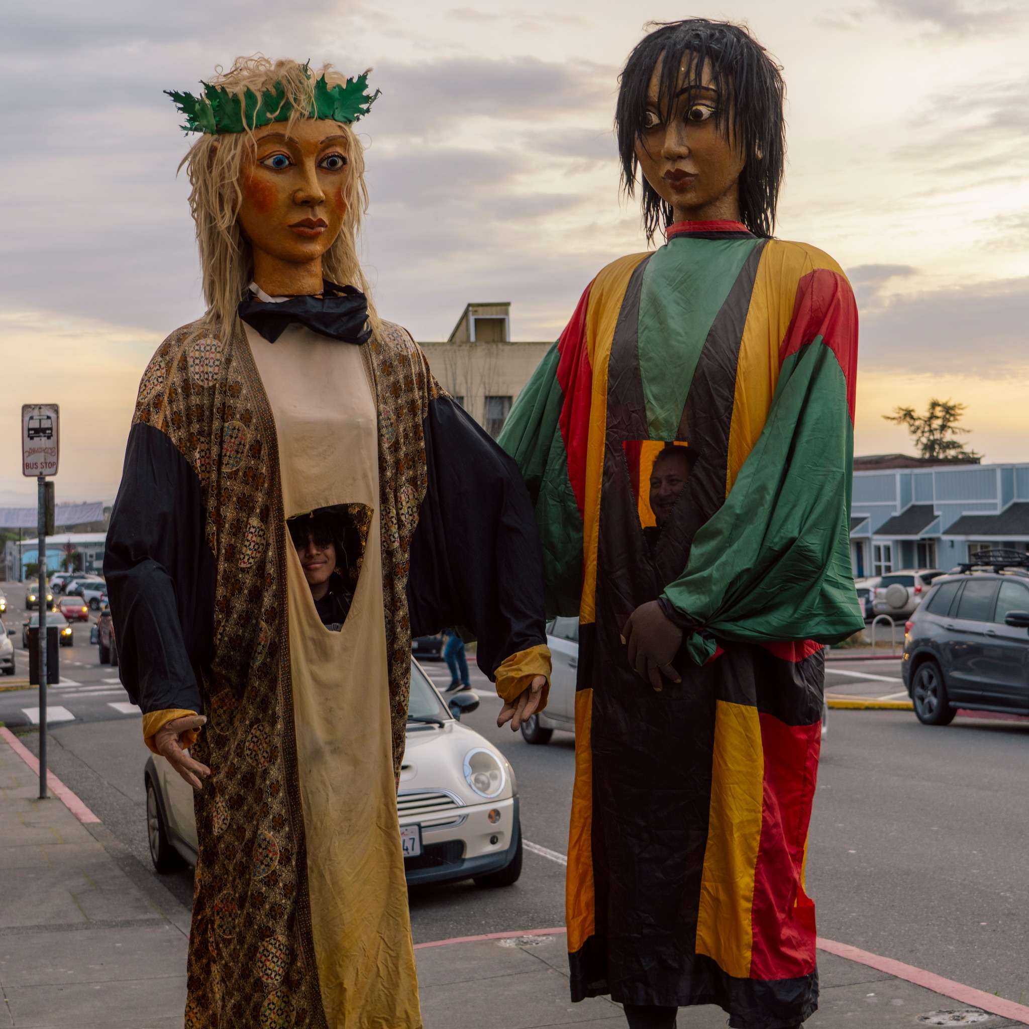 Two towering hand-made parade puppets on a downtown Arcata street at dusk