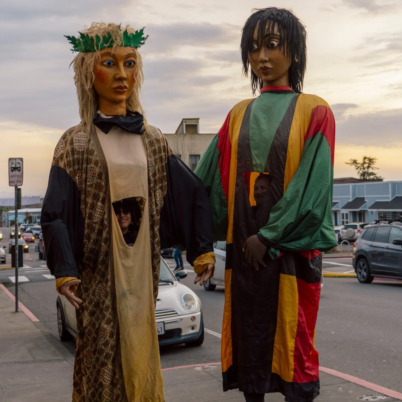 Two towering hand-made parade puppets on a downtown Arcata street at dusk