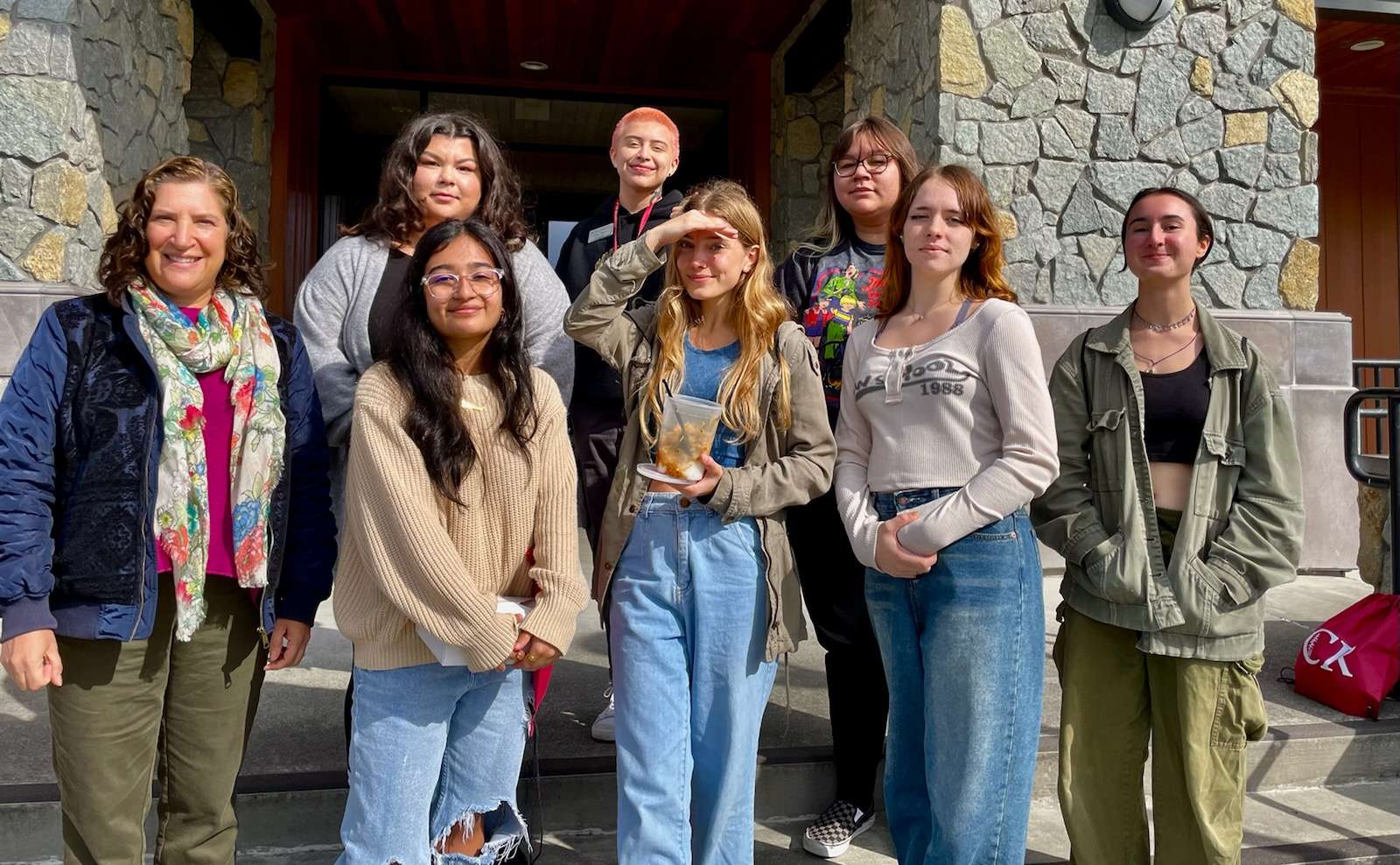 A group of nine students and a mentor posing on the steps outside a stone building