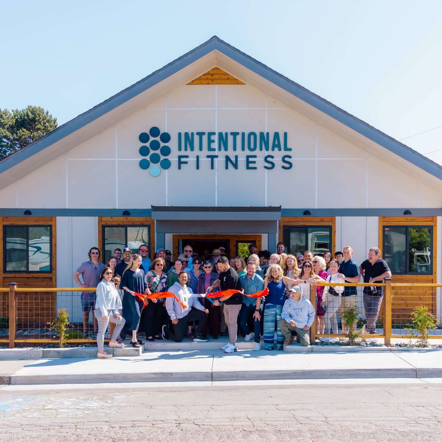 A crowd of Chamber members and neighbors cut a red ribbon in front of the new Intentional Fitness building
