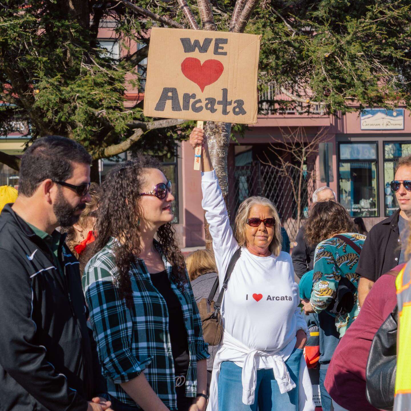 A woman in an “I ♥ Arcata” shirt holds up a hand-lettered “We ♥ Arcata” sign in a downtown crowd