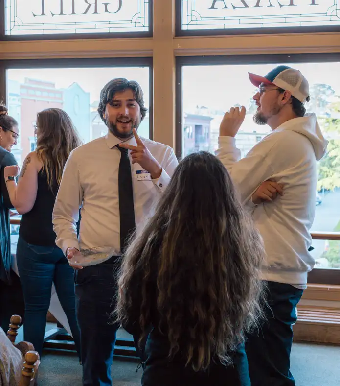 Three people talk at an Arcata Chamber of Commerce Young Professionals Network event: a man in business attire facing forward, a man in a sweatshirt facing to the side, and a woman with long hair
