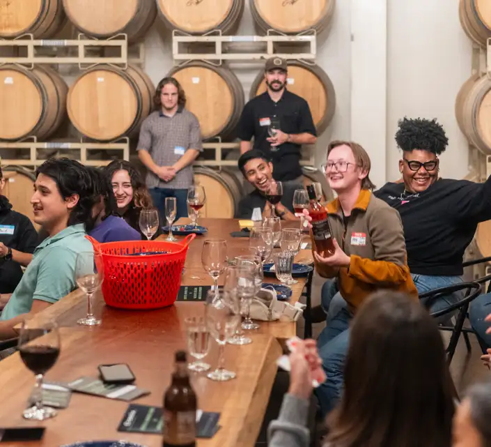 A group of people sit around a table, smiling, talking, and drinking wine and beer at an Arcata Chamber of Commerce Young Professionals Network event